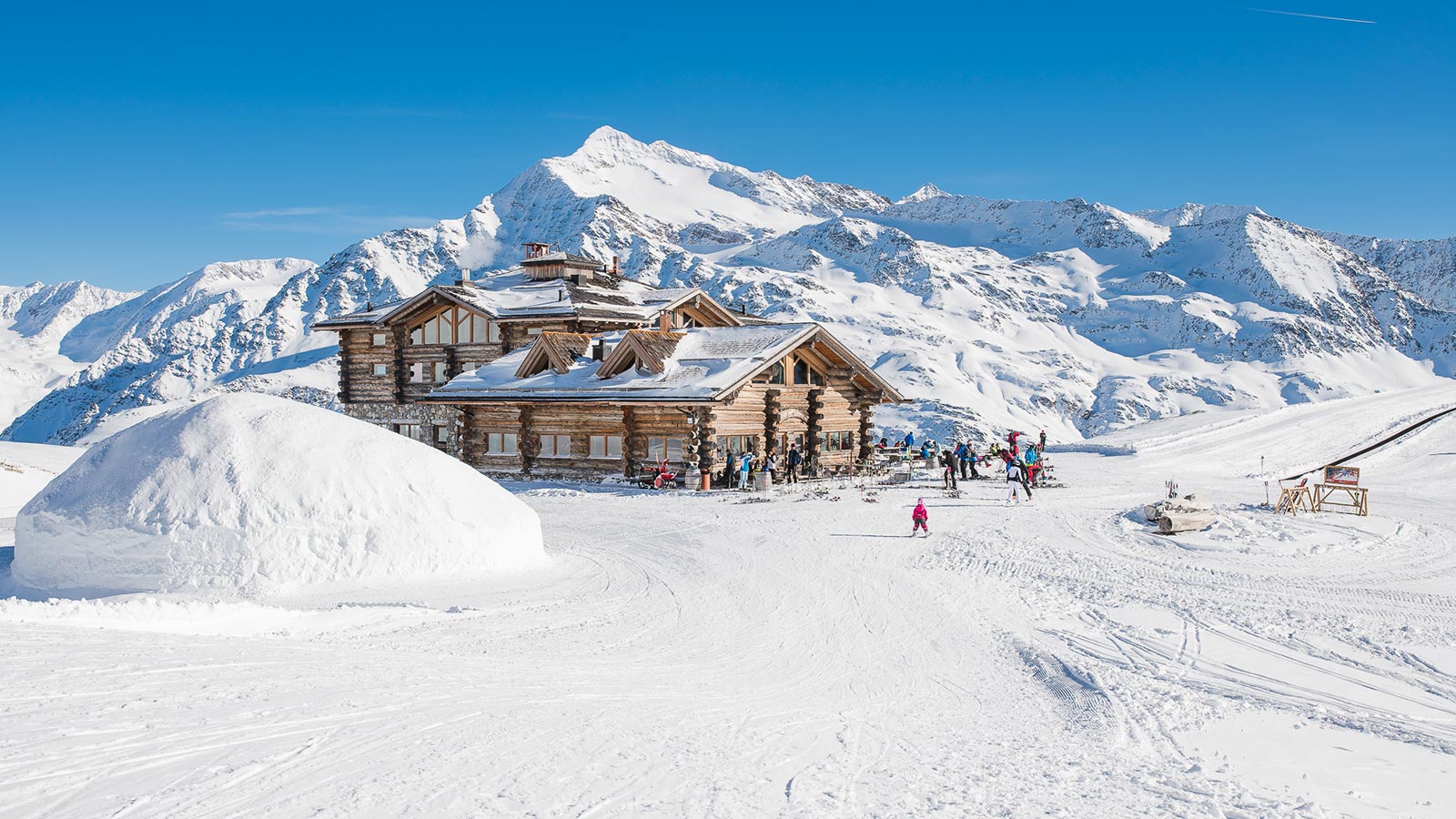 The mountain lodge during the day with a few skiers next to it